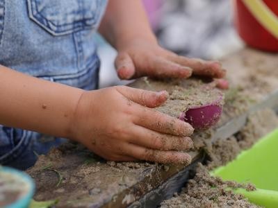 Kinderhände füllen Spielförmchen mit Sand.