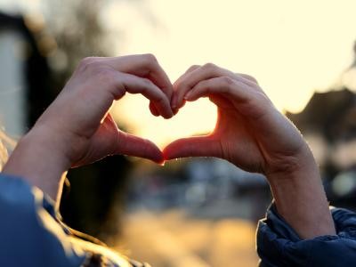 Hände formen ein Herz in der Abendsonne.