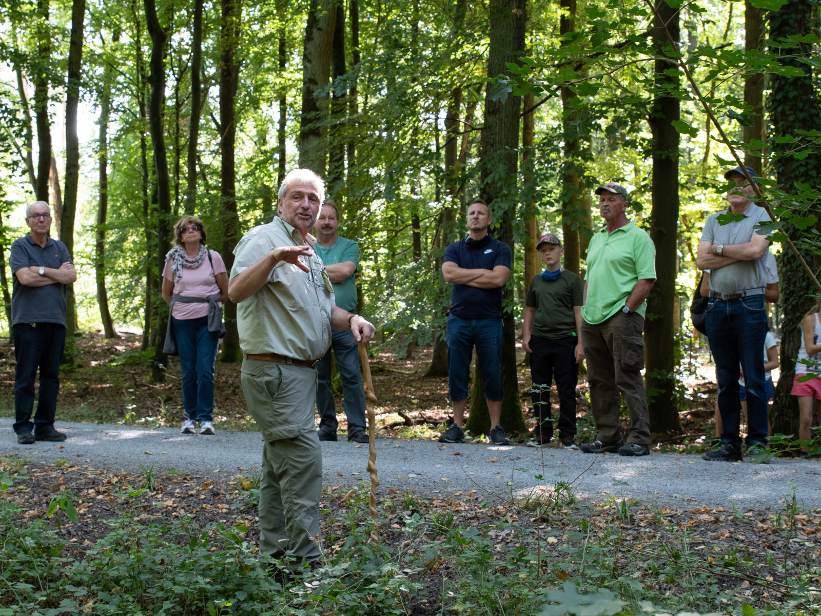 Menschen hören einem Förster zu, der im Wald etwas erklärt.