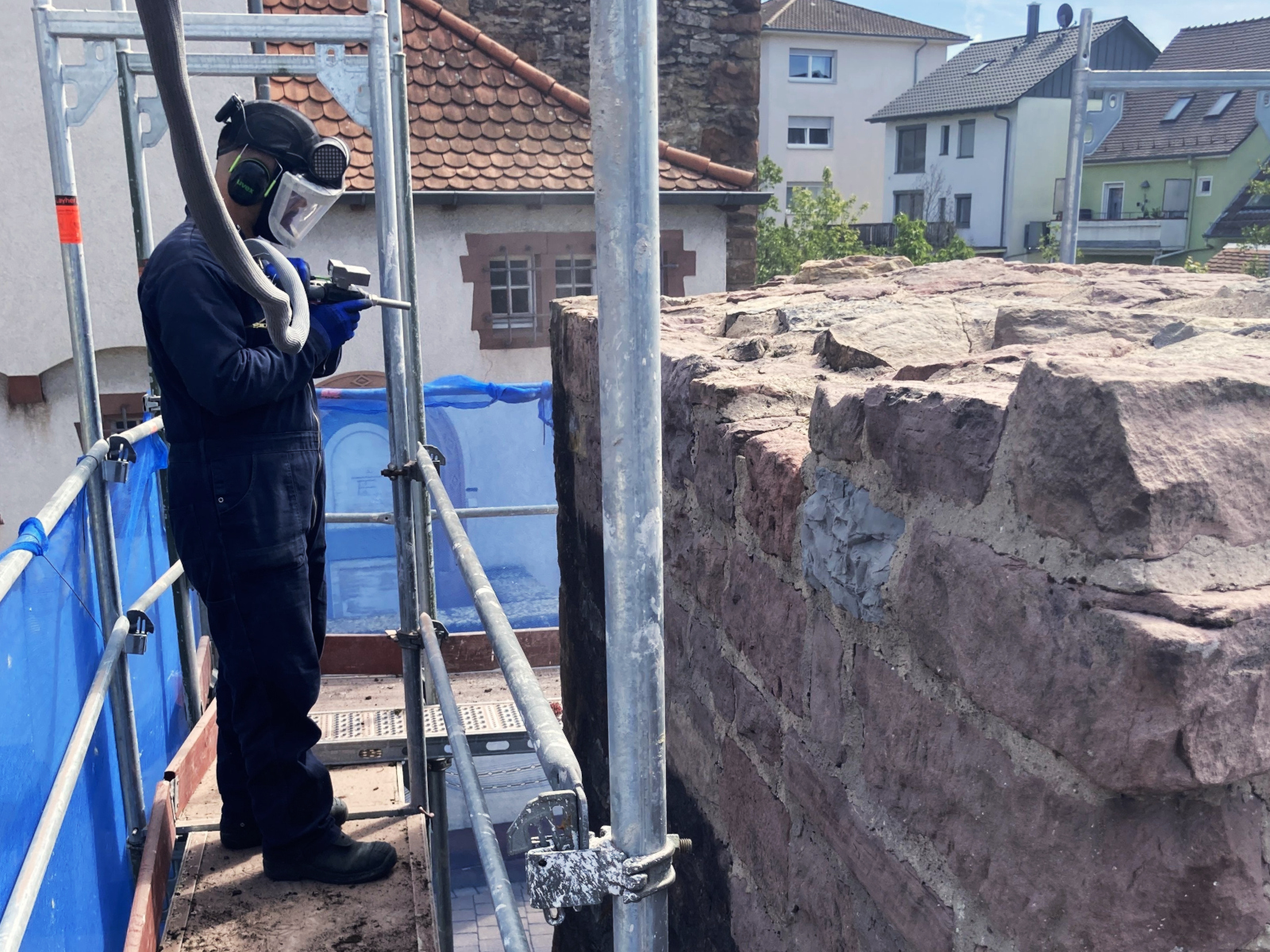 Arbeiter in Schutzkleidung steht auf einem Gerüst an der Stadtmauer. 
