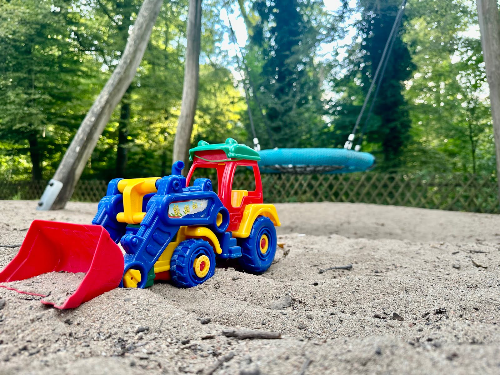 Bunter Spielzeug-Bagger im Sandbereich eines Spielplatzes.